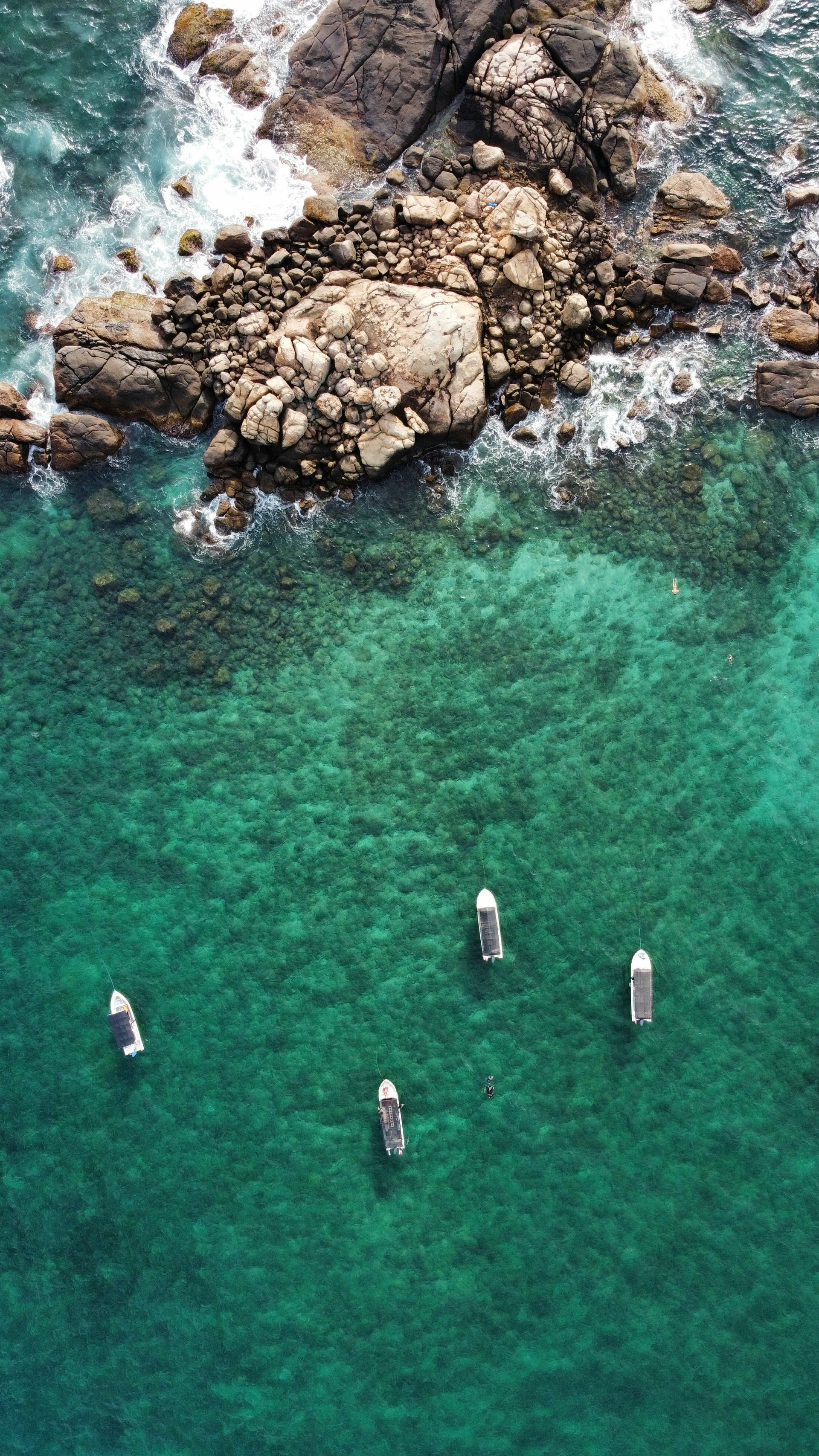 Aerial view of turquoise water with dive boats anchored near rocky coastline
