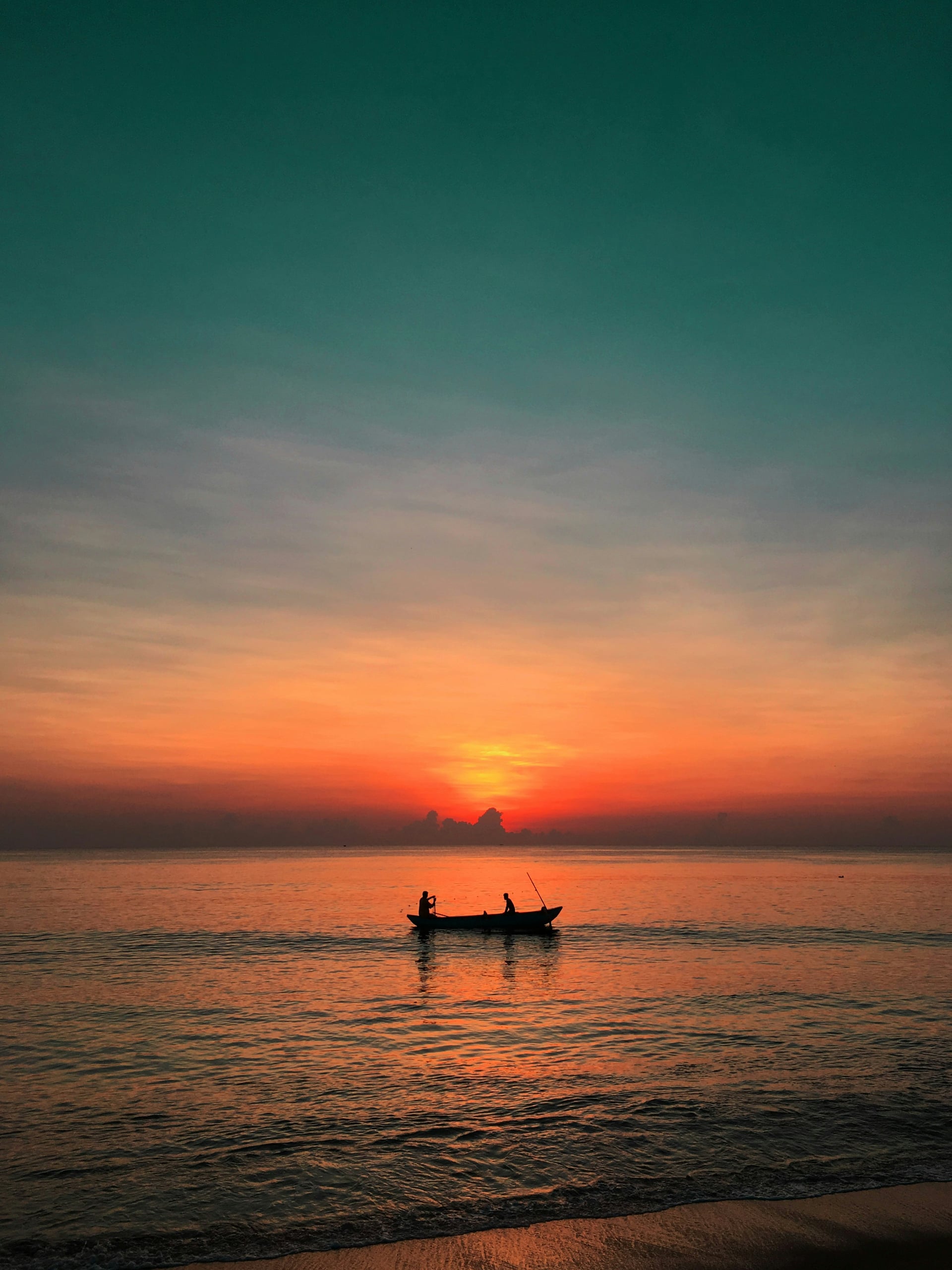 Fishing boat silhouette against a vibrant orange and pink sunset