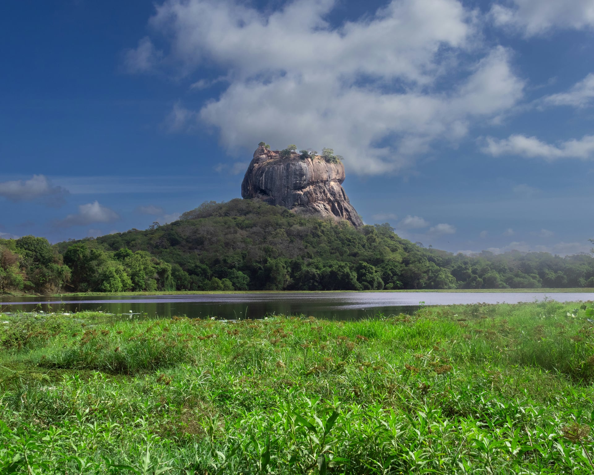 Sigiriya Rock Fortress with wetland lake in the foreground under blue sky