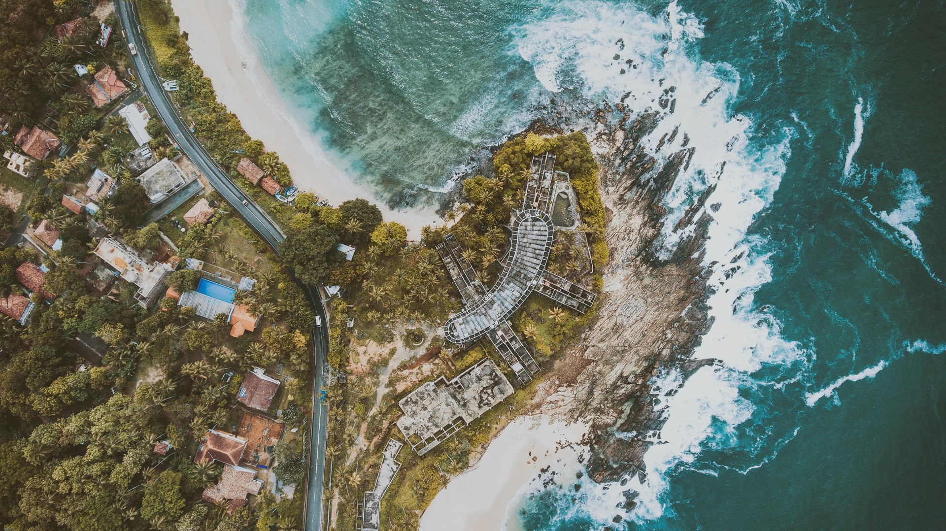 Aerial view of rocky coastal headland with ancient ruins and turquoise ocean
