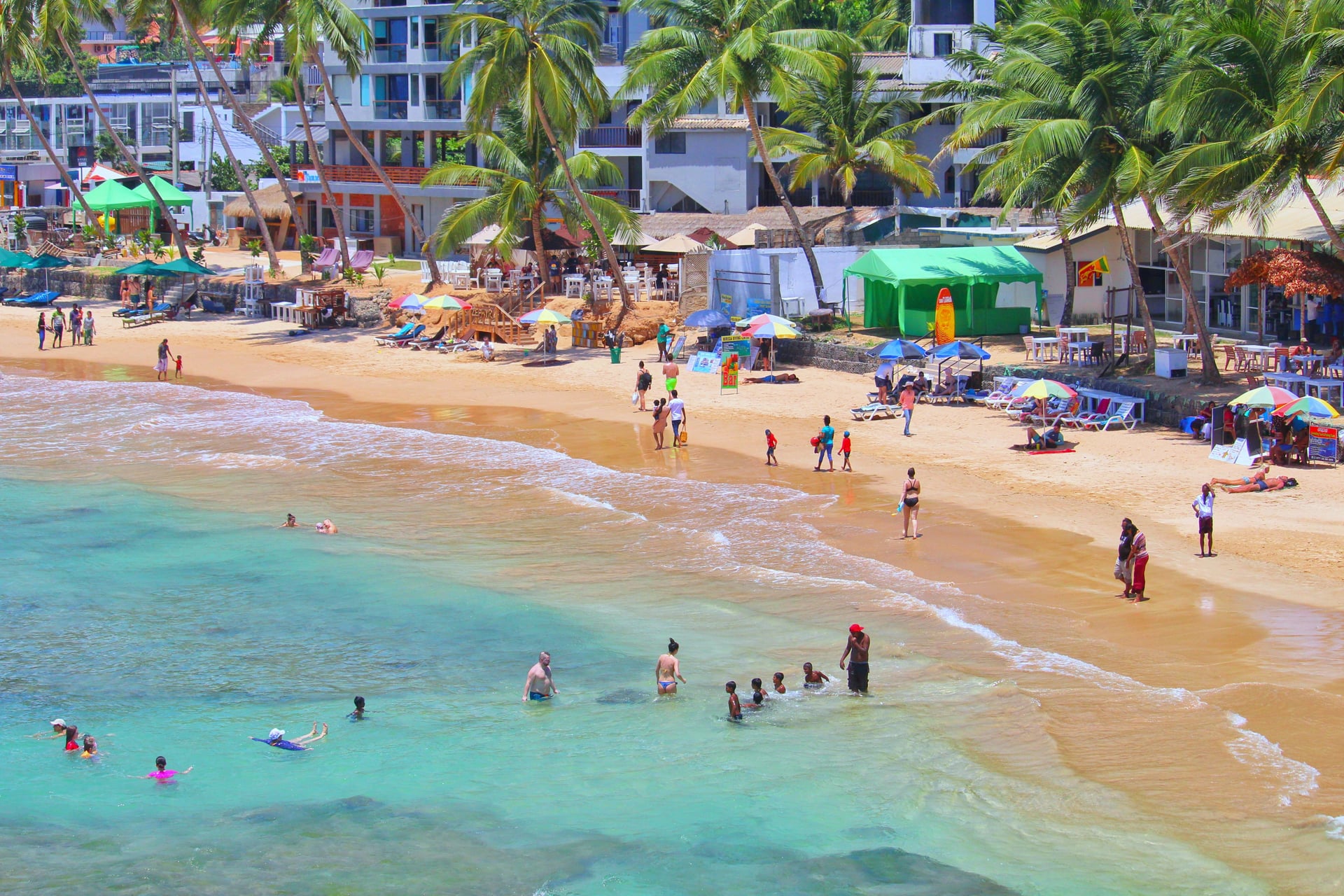 Hikkaduwa beach with swimmers in turquoise water and colourful beach shacks