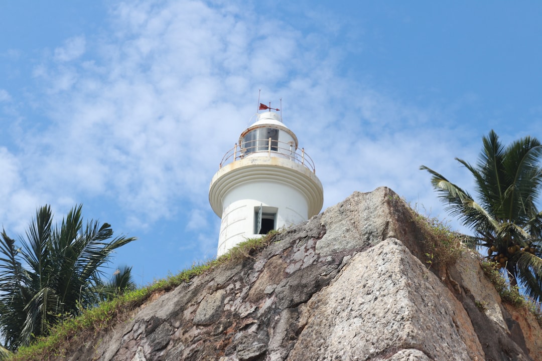 Close-up view of a lighthouse perched on a rocky cliff with palm trees